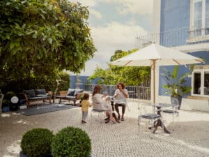 Eine frühstückende Familie auf der Dachterrasse eines Hauses unter einem freistehenden runden Holzsonnenschirm in Naturweiss sitzend von DolenzGollner.