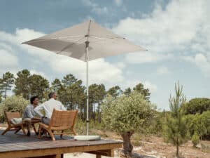 Zwei Männer sitzen auf Outdoor-Loungestühlen eines erhöhten Terrassenpodests, geschützt von einem freistehenden Alu-Sonnenschirm in Hellgrau von DolenzGollner.