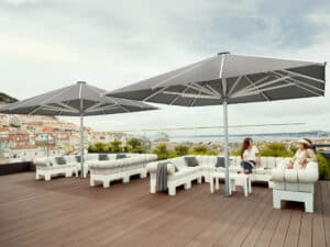 Dachterrasse eines Cafés und Restaurants mit großzügigen Outdoorbänken und zwei bodenverankerten, dunkelgrauen Alu-Sonnenschirmen von DolenzGollner.