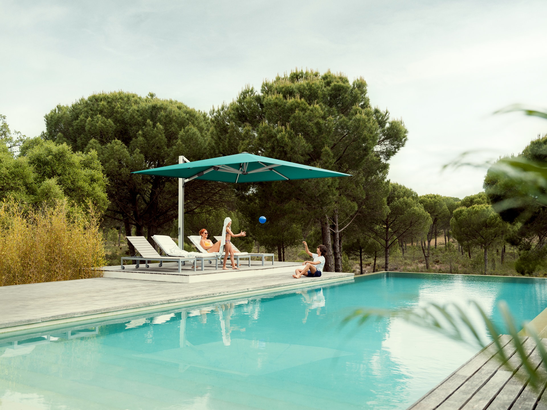 DolenzGollner Sonnenschutztechnik Ing. Wagner GmbH zeigt ein Badedeck neben einem Pool mit großem Sonnenschirm "Ambient Nova" in Türkis von Glatz.
