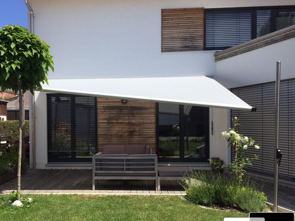 Ein an der Hausfassade montiertes, zum Garten leicht abgeneigtes Sonnensegel von DolenzGollner.