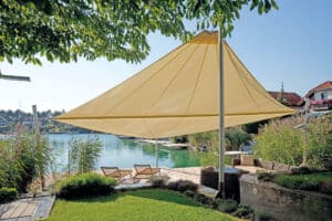 Ein rautenförmiges Sonnensegel in Gelb gespannt über Steg und Garten eines Grundstücks mit Seezugang von DolenzGollner.