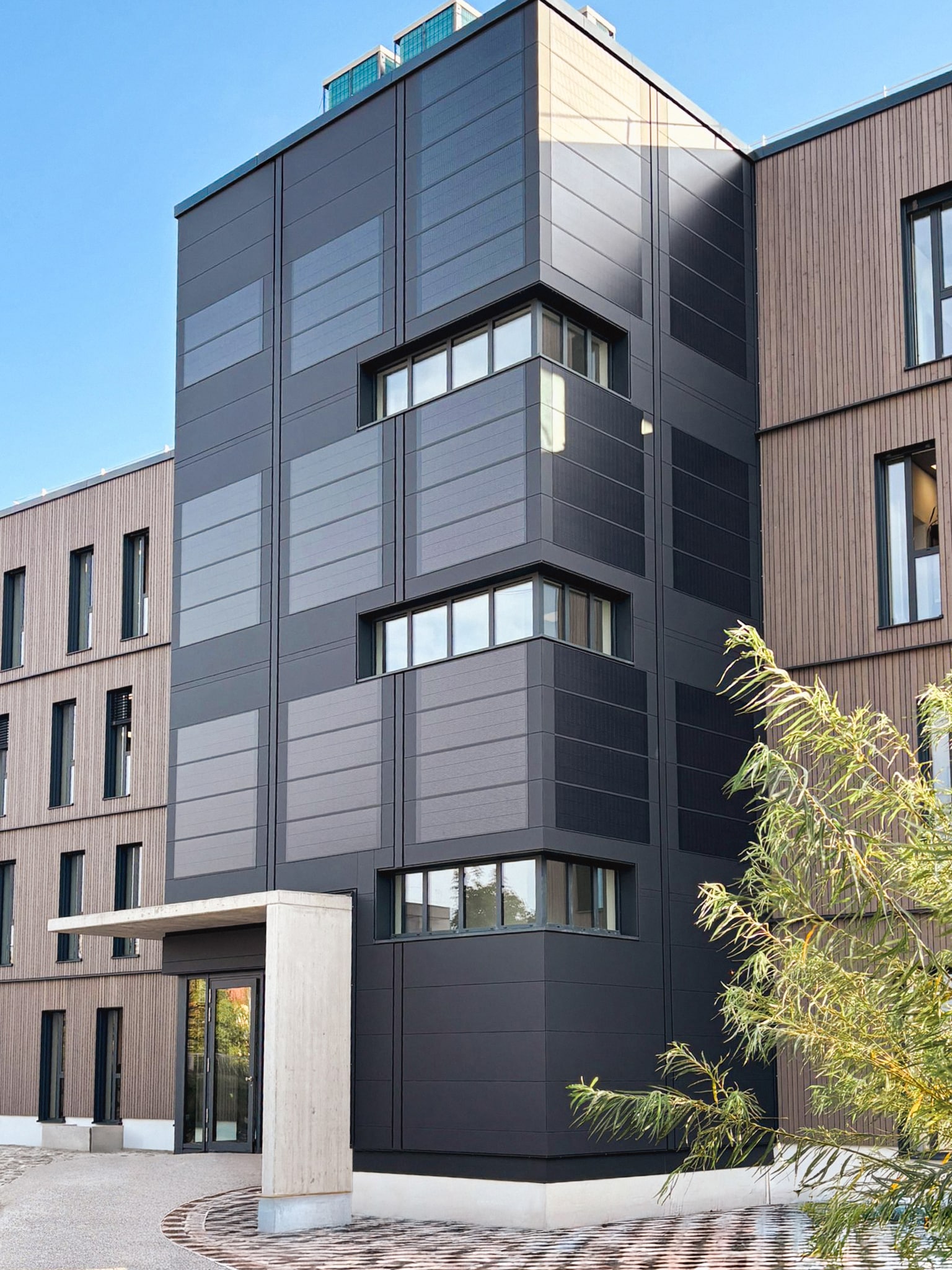 DOMICO zeigt die durchdringungsfreie Planum®Solar-Fassade: 210 m² Planum®-Fassade, Deckbreite 600 mm, RAL 7016 oder 7021 matt, 108 m² Planum®Solar mit Glasoberfläche.