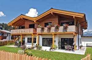 ERLER Haus zeigt ein schönes, rustikales Holzhaus mit großem Balkon und einer überdachten Terrasse mit gemütlichen Möbeln und vielen Pflanzen.