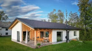 Einfamilienbungalow mit Satteldach, Fassadenelementen aus Holz, einer überdachten Terrasse mit Podest und bodentiefen Fenstern von ERLER Haus.