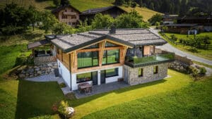 Einfamilienhaus mit erweitertem Satteldach, Steinfassade, Fassadenelementen aus Glas und einem Rund-um-Balkon mit Nurglasgeländer von ERLER Haus.
