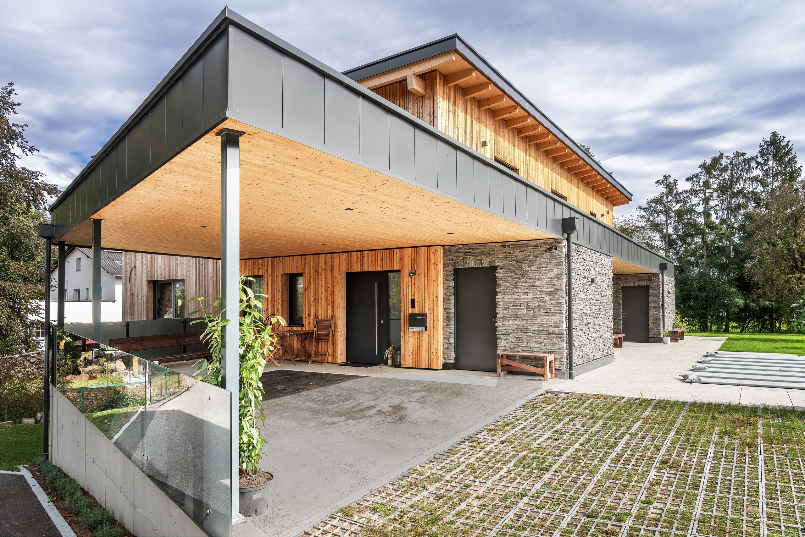Überdachter Eingangsbereich und Carport eines Einfamilienhauses mit einer Mischung aus Holzfassade- und Steinfassadenelementen von ERLER Haus.