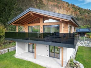 Überdachter Eckbalkon eines Einfamilienhauses mit Balkonschiebetüren mit schwarzem Alurahmen, Holzfassade und Nurglasgeländer in Schwarz von ERLER Haus.
