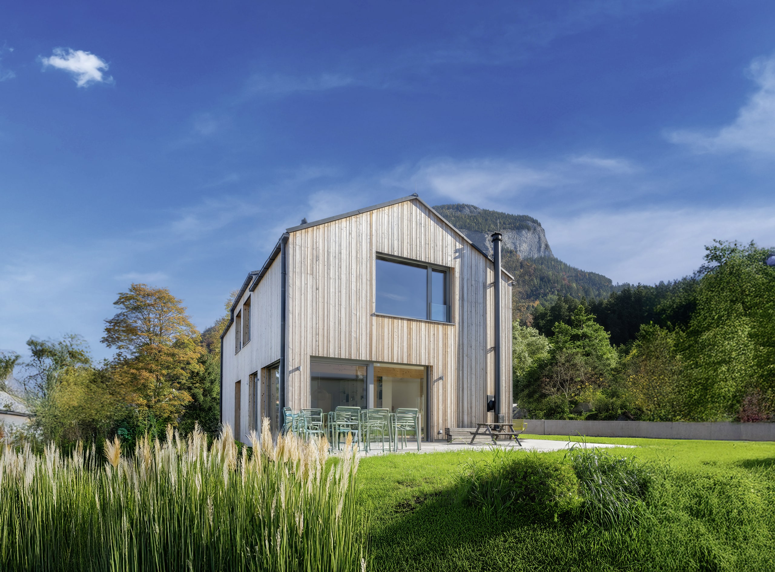 Einfamilienhaus mit Satteldach und vertikaler Holzsprossenverkleidung, mehreren Terrassenschiebetüren, bodenlosen Fenstern und hölzernem Terrassenpodest mit Outdoormöbeln von ERLER Haus.