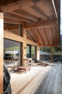 Überdachter Balkon eines Einfamilienhauses mit Balkonschiebetüren mit schwarzem Alurahmen, Holzdielen und Holzfassade von ERLER Haus.