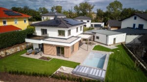 Einfamilienhaus mit Walmdach, Holzsprossenfassade im Erdgeschoß, Mauerwerk mit Rauchglasbalkon im ersten Stock, überdachter Terrassenbereich und Pergola mit Lamellendach von ERLER Haus.