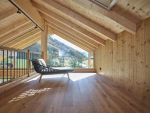 Ein offener Galeriebereich mit Dachschräge, Balken, Chaiselongue, und einem Glaselement für die perfekte Aussischt von ERLER Haus.