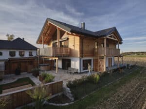 Außenansicht eines Holzhauses mit Steinfliesen und einen durch zwei Holzbalkone überdachter Terrassenbereich von ERLER Haus.