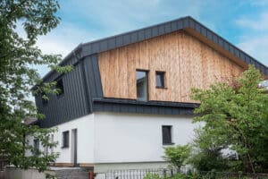 Ein Haus mit Satteldach und Fassadenelementen aus Blech und Holz, klaren Linien, kontrastreicher Materialwirkung und moderner Außenästhetik von ERLER Haus.