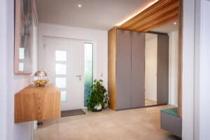 Ein einladender Eingangsbereich mit Garderobe und einem indirekt beleuchteten Deckenpaneel aus Holzsprossen von ERLER Haus.