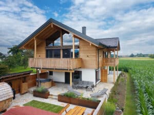 Außenansicht eines Holzhauses mit Garten- und Terrassenbereich, zwei großzügigen Balkonen, Holz-Alu‑Fenstern, Sauna, Whirlpool und harmonischer Landschaftsanbindung von ERLER Haus.
