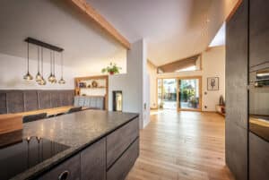 Eine offene Wohnküche mit Essbereich und Blick auf den überdachten Balkon durch helle Holz-Alu-Balkonschiebetüren und passendem Oberlicht von ERLER  Haus.