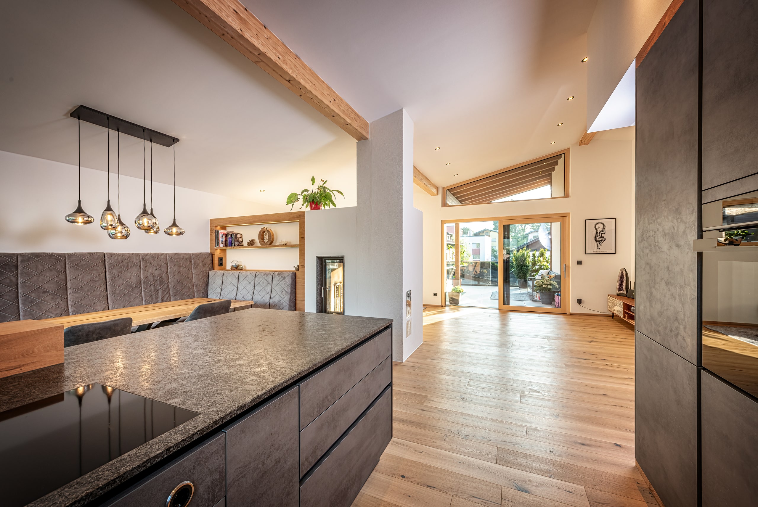 Eine offene Wohnküche mit Essbereich und Blick auf den überdachten Balkon durch helle Holz-Alu-Balkonschiebetüren und passendem Oberlicht von ERLER  Haus.