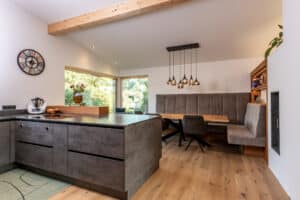 Ein offener Wohn‑ und Essbereich mit Deckenbalken, Dachschräge, gemütlichem Sitzfenster und großen Glaselementen und harmonischer Verbindung von Koch‑ und Esszone von ERLER  Haus.