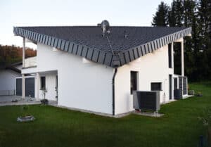Ein Einfamilienhaus mit Kombinationsdach, überdachtem Eingangsbereich, Wärmepumpe, Doppelgarage und grüner Rasenfläche von ERLER Haus.