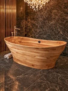 Festwood zeigt eine freistehende Badewanne aus hellem Holz und Messing Armatur in einem edlen Badezimmer mit dunklen Mamorfliesen.