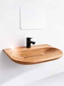 Festwood zeigt ein Waschbecken aus hellem Holz mit länglichem Wasserablauf aus Holz und schwarzer Armatur an der Wand montiert.
