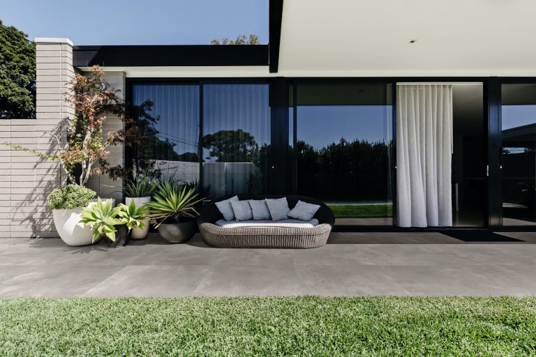 Fliesendorf zeigt eine überdachte Terrasse mit einer gemütlichen Rattanlounge, vielen exotischen Pflanzen und großen Fensterflächen.