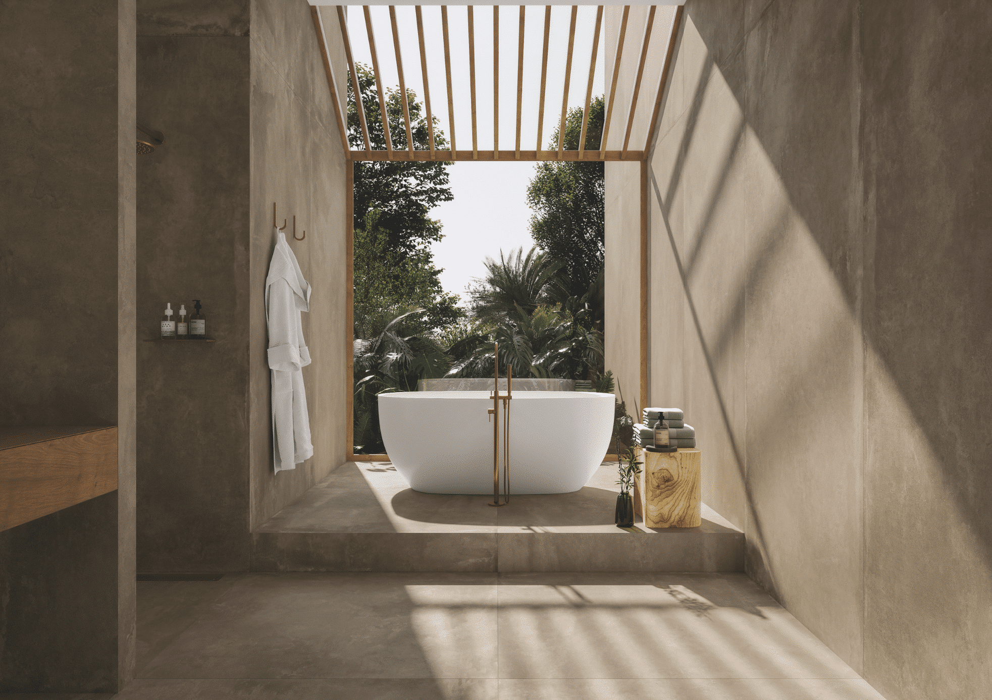 Fliesendorf zeigt eine weisse, freistehende Badewanne mit goldenen Armaturen im gefliesten Außenbereich in Naturtönen mit Blick auf den Garten.