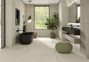 Fliesendorf zeigt warmes Badezimmer mit großformatigen Bodenfliesen in Naturtönen, freistehende schwarze Badewanne und schwarzes Doppelwaschbecken.