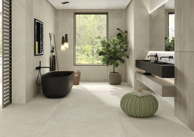 Fliesendorf zeigt warmes Badezimmer mit großformatigen Bodenfliesen in Naturtönen, freistehende schwarze Badewanne und schwarzes Doppelwaschbecken.
