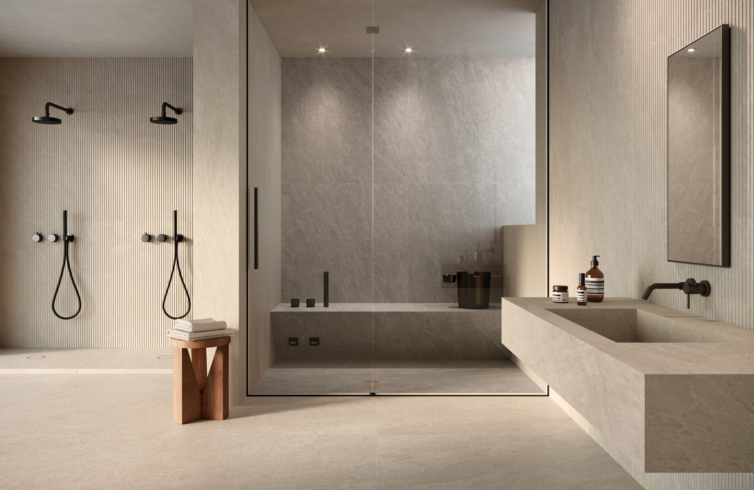 Fliesendorf zeigt ein Wellness-Badezimmer mit großformatigen, fugenlosen Boden- und Wandfliesen in grau-beiger Steinoptik, einem passenden schwebenden Waschtisch, zwei seperate Regenduschen mit Armatur und Stabbrause in Schwarz und eine Steinsauna mit Glastür.