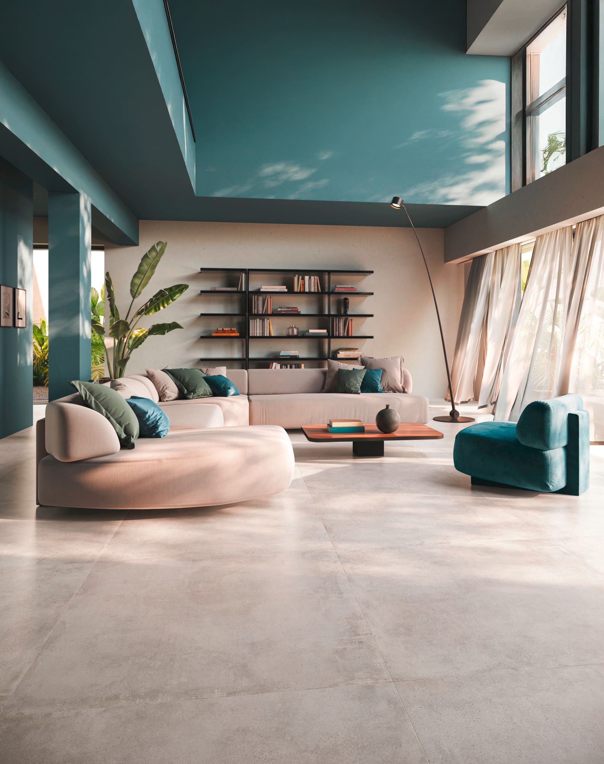 Fliesendorf zeigt einen offenen Wohnraum mit Loftcharakter mit beigem Sofa und Loungesessel, Accessoires und Wänden in Petrol und einer grossformatigen Bodenfliese in beiger Steinoptik.