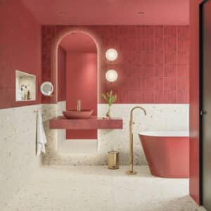Fliesendorf zeigt ein Badezimmer mit Bronze-Armaturen, Steinwaschtisch, freistehender Badewanne, roten Stabfliesen und XXL-Fliesen in Terrazzo-Optik an Wand und Boden.