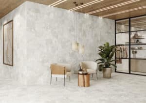 Warte- bzw. Wohnbereich mit großformatigen hellen Steinfliesen an Wand und Boden im aus der Gravina-Reihe von Fliesendorf mit einer Deckenverkleidung, Beistelltisch und Accessoires aus Holz für einen abgerundeten Look.