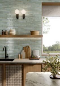 Küche mit hellblauen horizontal verlegten Stabfliesen mit Patina als Küchenrückwand aus der Life-Reihe von Fliesendorf, kombiniert mit warmen Holzelementen, Küchenfronten aus Geflecht und einer weissen Marmorarbeitsplatte.