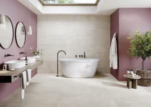Badezimmer mit großformatigen beigen Steinfliesen an Wand und Boden aus der Portland-Rock-Reihe von Fliesendorf, kombiniert mit beerenfarbenen Wänden, schwarzen Armaturen und natürlichen Holzelementen.