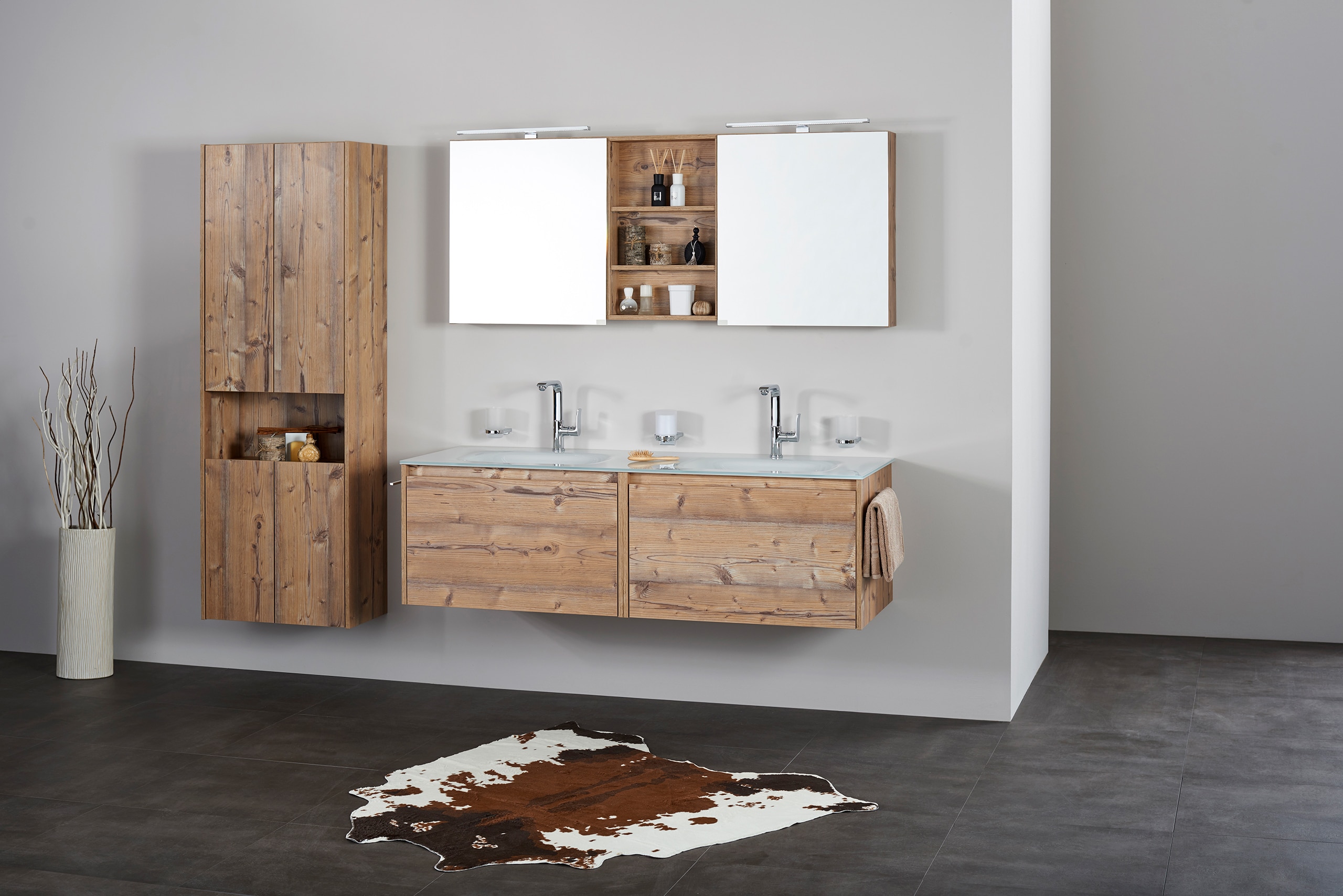 Frauenthal Handel zeigt ein Badezimmer mit Doppelwaschbecken, Unterschrank aus rustikalem Holz mit zwei großen Schubladen, Hochschrank und einem Spiegelschrank mit zwei Türen, offenen Ablagefächern und Beleuchtung.