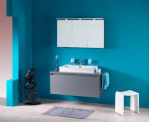 Frauenthal Handel zeigt ein Badezimmer mit einem aufgesetztem Waschbecken, dunkelgrauem Unterschrank mit einer großen Schublade und einem eleganten Spiegelschrank mit drei Türen und Beleuchtung.