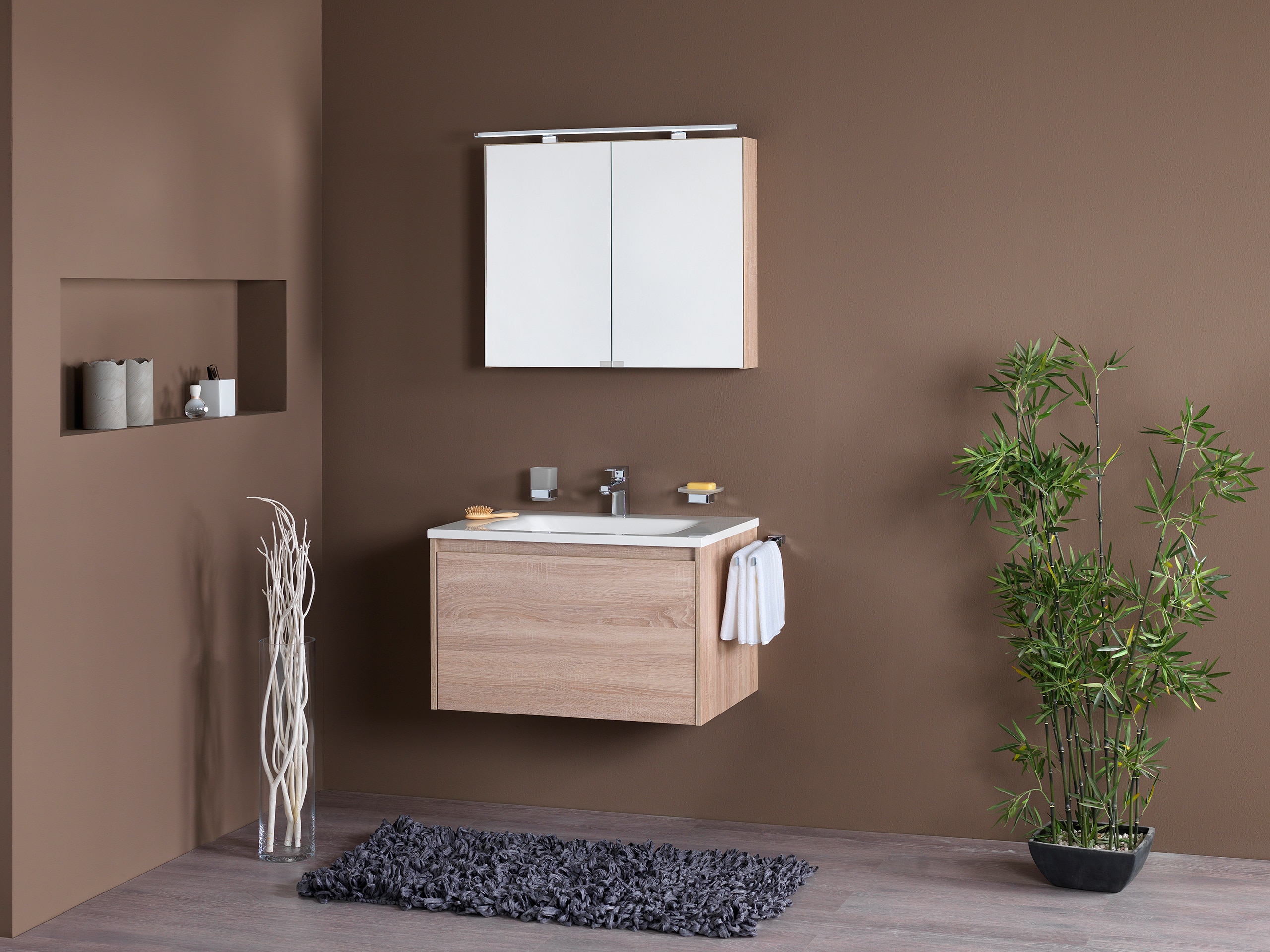 Frauenthal Handel zeigt ein Badezimmer mit einem Waschbecken, Unterschrank aus hellem Holz mit einer großen Schublade und einem eleganten Spiegelschrank mit Beleuchtung.