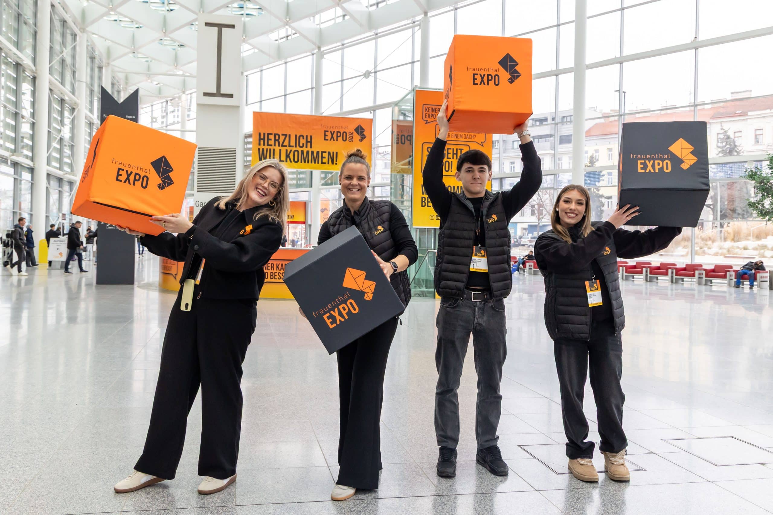 Mitarbeiter der Frauenthal EXPO Messe halten Würfen mit dem Logo der Messe in den Händen und stehen in der Eingangshalle.