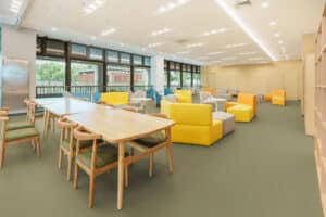 Gerflor präsentiert einen großen hellen Raum mit vielen Sitzgelegenheit, großen Fensterflächen und einem mit Lino beschichteten Boden in einem Grünton.