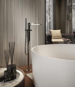 GESSI präsentiert eine freistehende Badewanne mit freistehender Armatur in chrom mit gerilltem Drehhebel und integrierter stabförmigen Handdusche.