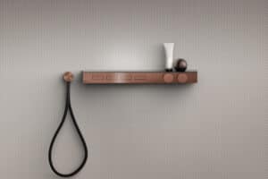 GESSI zeigt eine Bedienleiste in Kupfer an einer Duschwand mit Tasten für Duscheinstellungen und zwei Drehreglern für ein Musik.