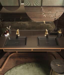 GESSI zeigt einen Doppelwaschtisch mit versenkten schwarzen Waschbecken mit dahinterstehender goldener Armatur.