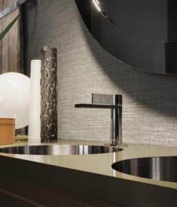 GESSI zeigt ein flächenbündiges, metallisches Waschbecken mit freistehender Armatur aus chrom mit aufgerauhtem Drehhebel.