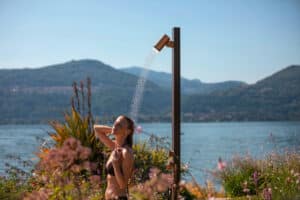 GESSI zeigt eine Frau, die sich im Freien mit der freistehenden kupferfarbenen Duschsäule duscht.