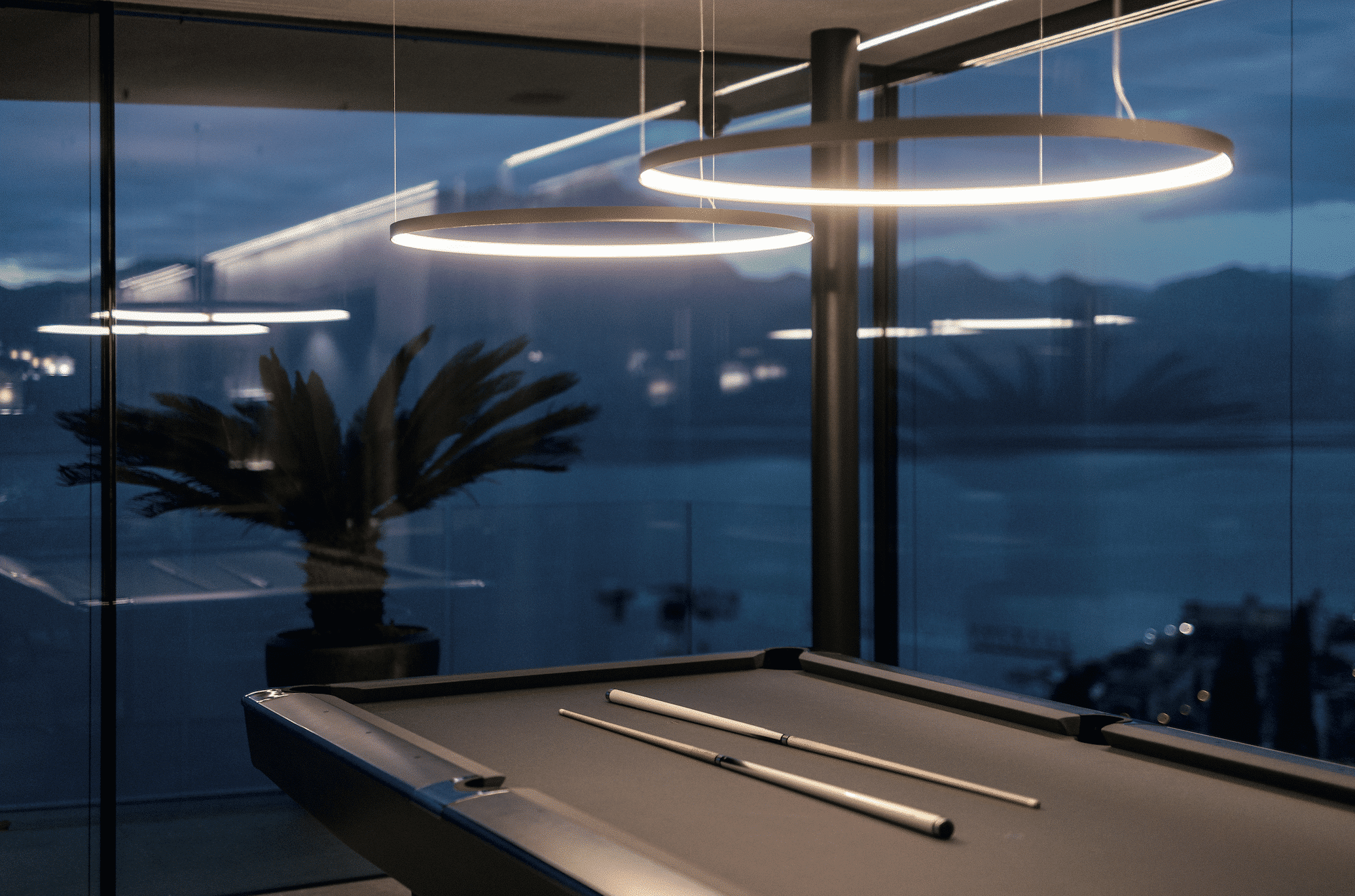Gira zeigt einen schwarzen Billardtisch mit eleganten, runden Hängelampen darüber, die man mit SmartHome Lichtsteuerung bedienen kann.