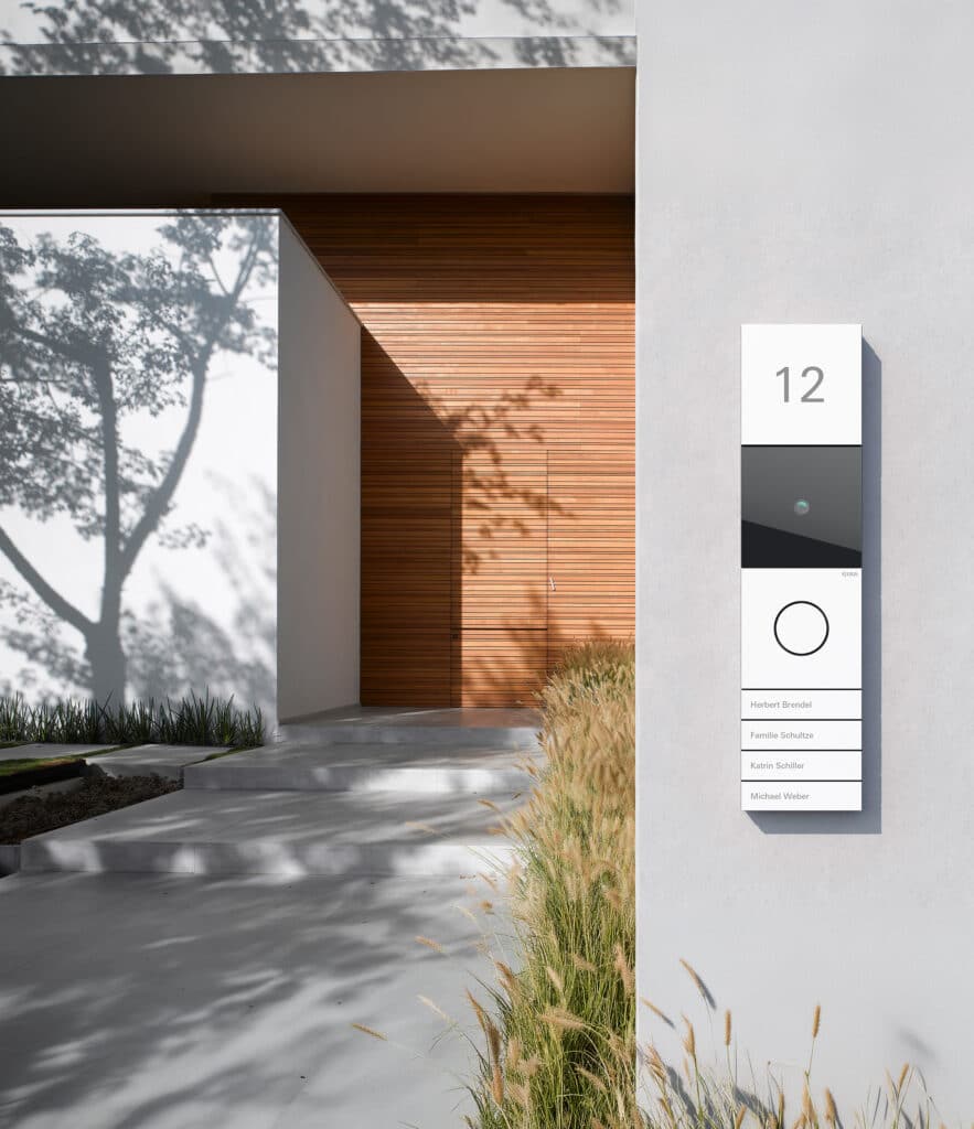 GIRA zeigt einen Eingangsbereich mit einer an der Wand installierten Gegensprechanlage inklusive Kameramodul.