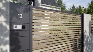 GIRA zeigt eine Toreinfahrt mit einer silbernen Außenanlage mit schwarzem Kameramodul, Fingerprint-Key und Gegensprechanlage.