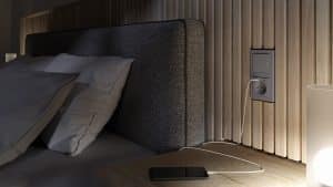 GIRA präsentiert ein Schlafzimmer mit Lichtschalter, der den Schaltzustand via Kontrolllampen anzeigt und darunter eine Steckdose mit USB-Anschluß zum Auflade eines Mobiltelefones.